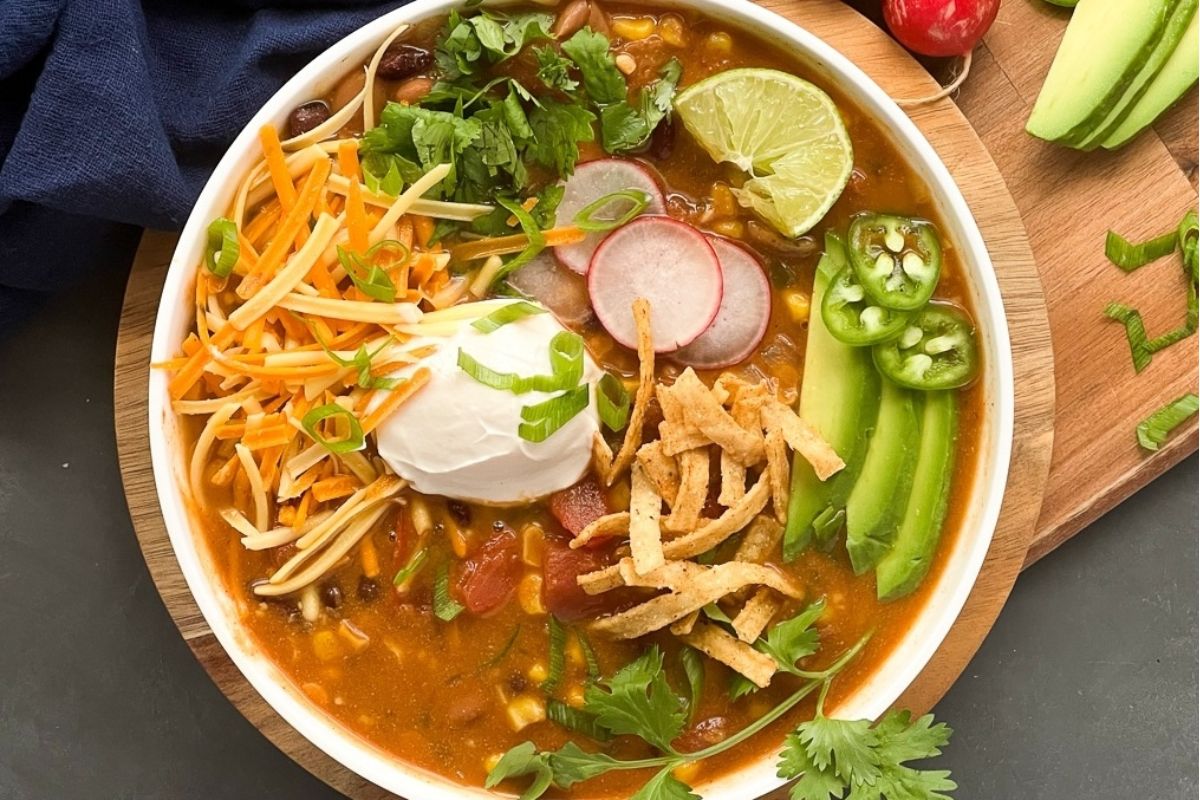 A bowl of taco-flavored Mexican soup with sour cream and avocado.