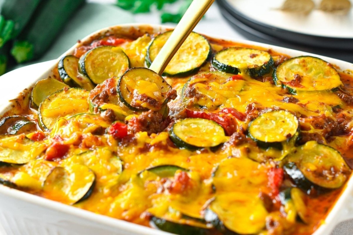 Baked zucchini and tomato casserole topped with melted cheese, served in a white dish.