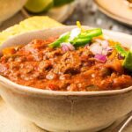 A bowl of bean-free chili with cornbread on the table.