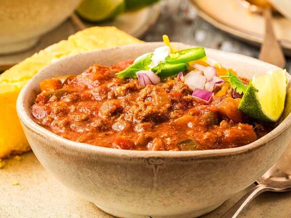 A bowl of bean-free chili with cornbread on the table.