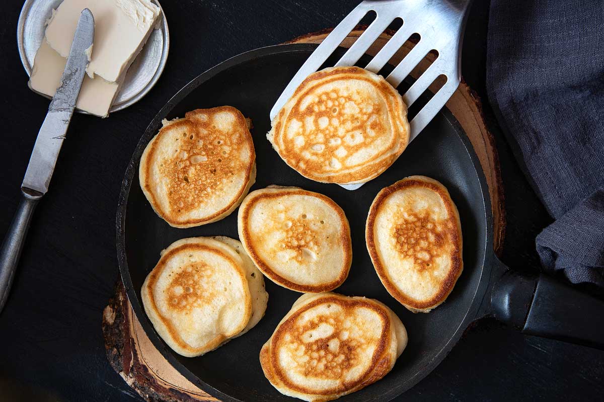 Small pancakes in a pan on a wooden board.