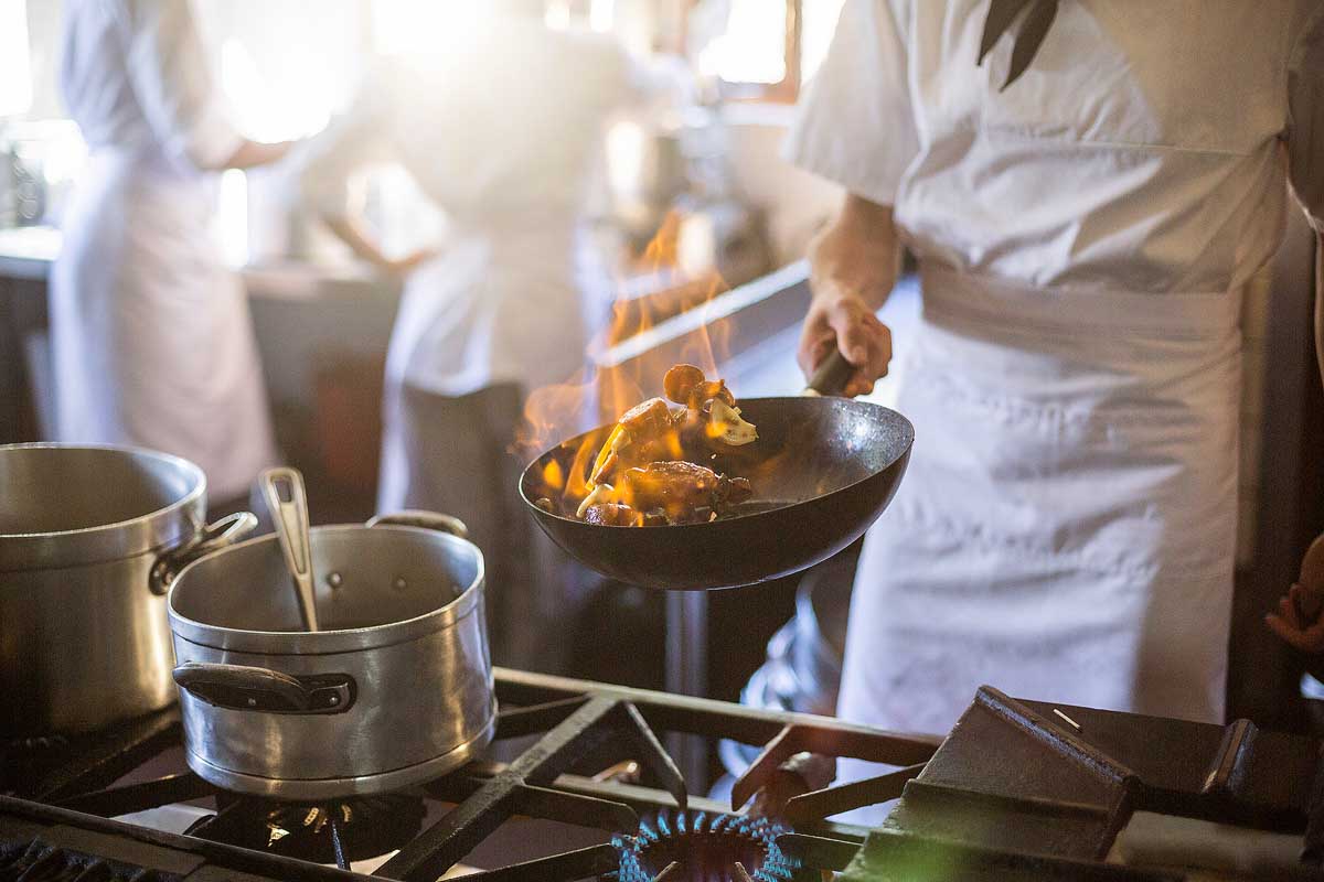 Mid section of chef tossing stir fry over large flame in commercial kitchen