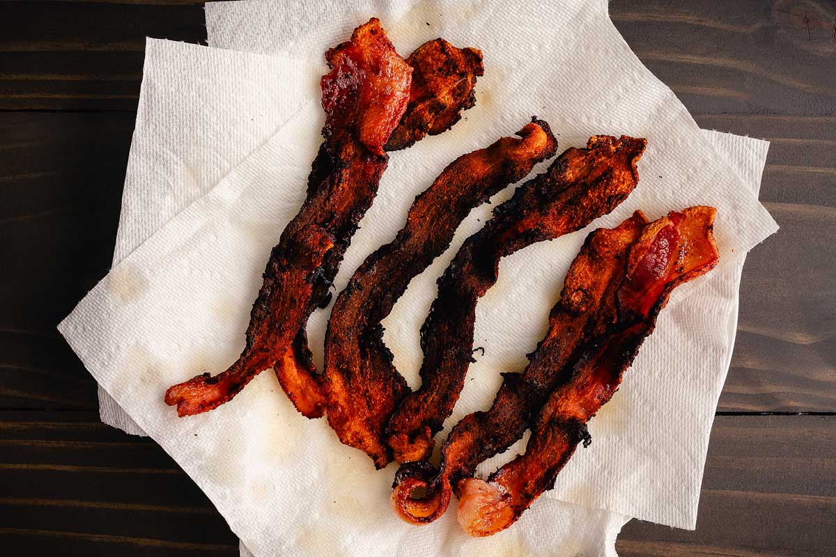 Overcooked Bacon Draining on Paper Towels: Strips of burned thick cut streaky bacon draining on kitchen roll