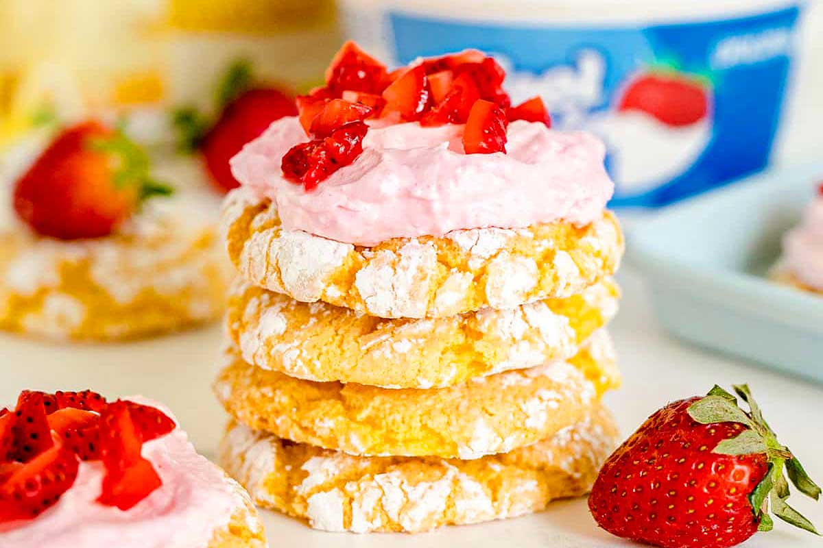 A stack of powdered Valentine's Day cookies topped with pink cream and chopped strawberries, surrounded by fresh strawberries.