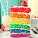 A slice of colorful rainbow layer cake on a white plate.