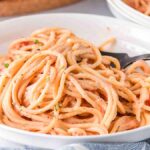 A plate of spaghetti with a fork and pink pasta sauce.