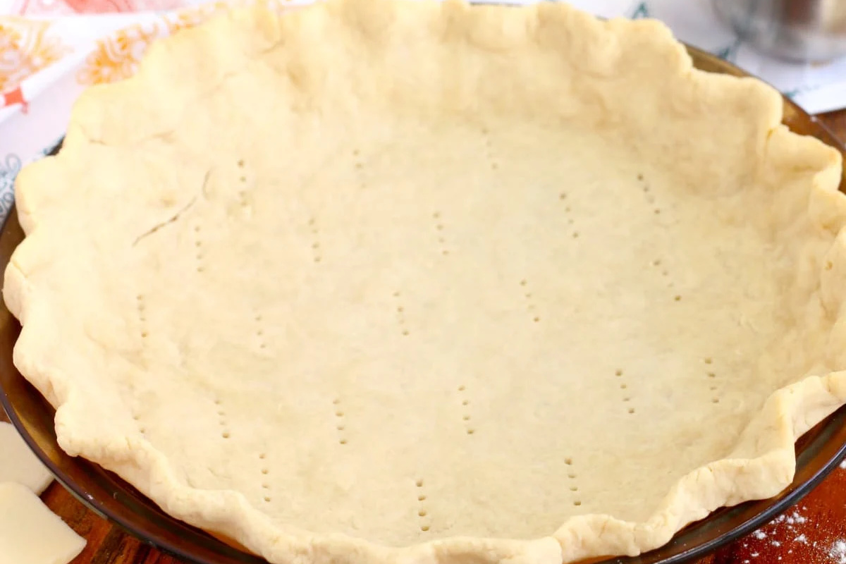Unbaked pie crust in a glass dish, docked with fork holes for pie recipes.