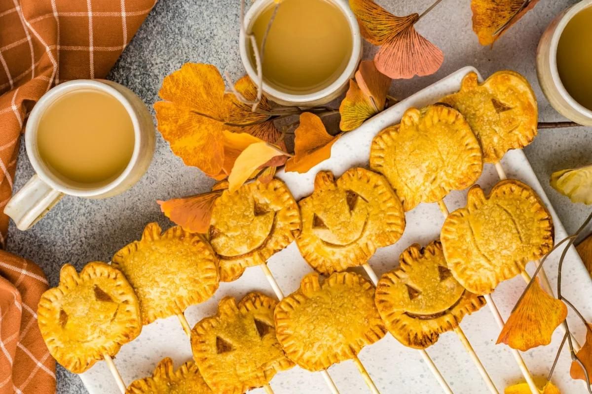 Autumn-themed mini pie recipes with leaf designs served with cups of apple cider.