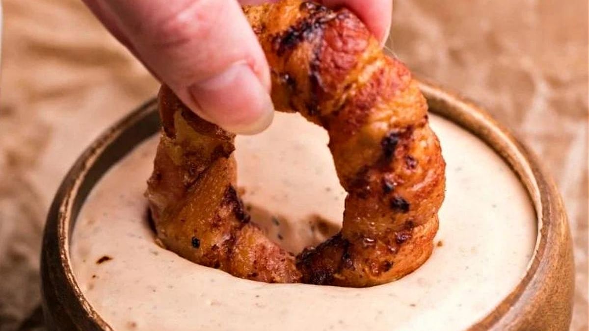 A hand dipping a grilled shrimp into a bowl of creamy sauce, perfect for air fryer recipes.
