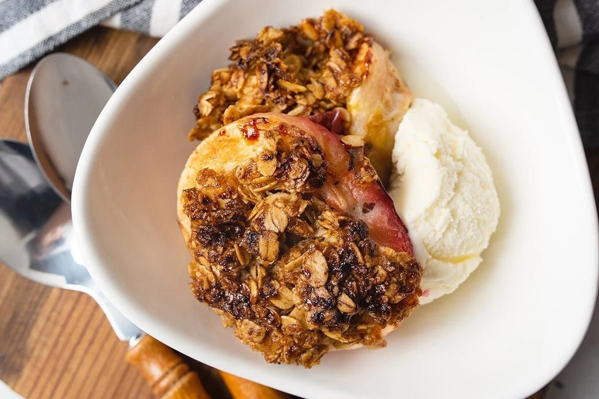 A bowl containing baked apples with a crumble topping, served alongside a scoop of vanilla ice cream, perfect for Father's Day breakfast.