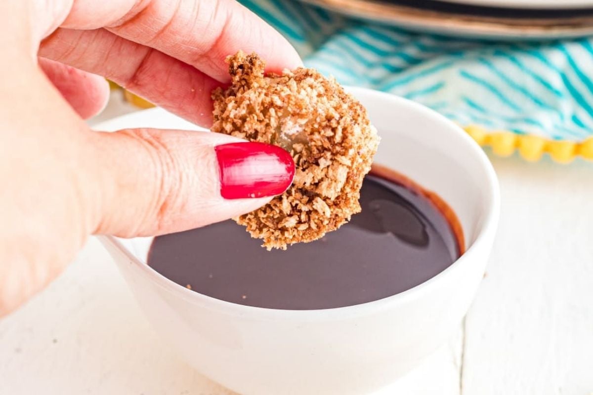 A person dipping a cookie into a bowl of air fryer chocolate sauce.