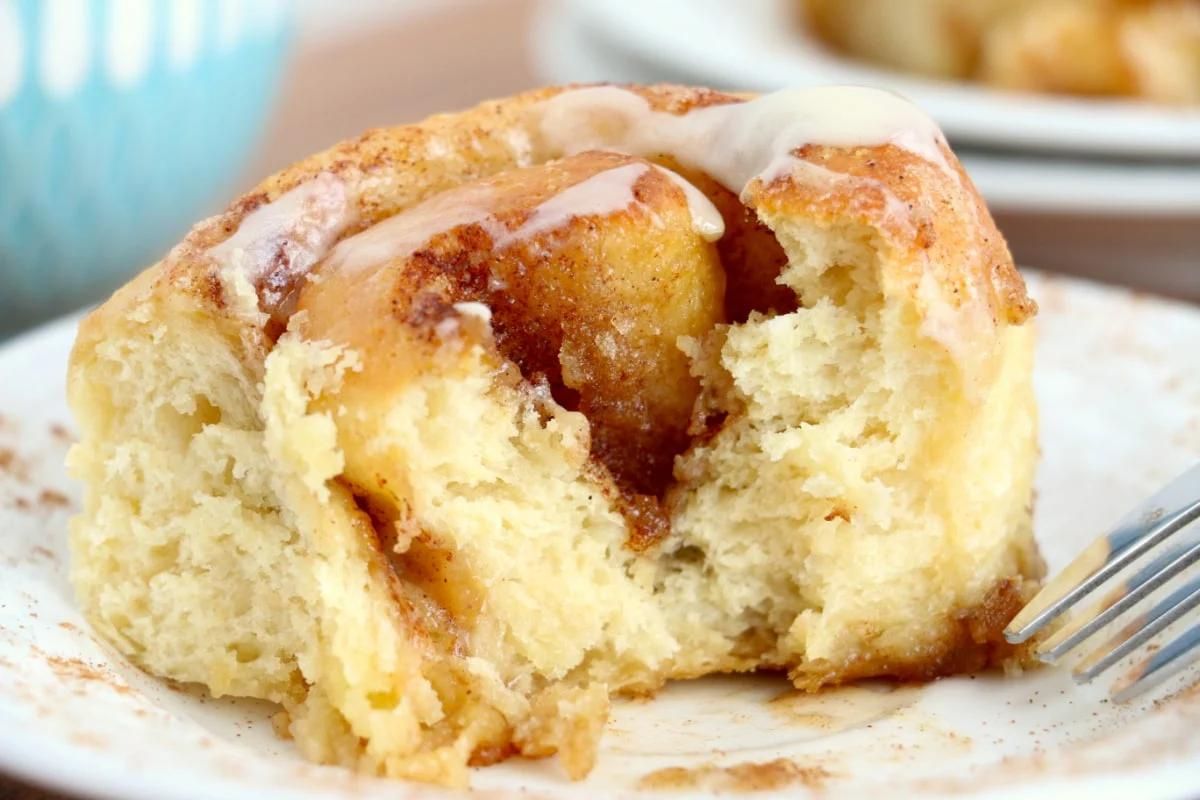 A close-up of a cinnamon roll, partially eaten, with icing on a plate, perfect for showcasing cinnamon roll recipes.