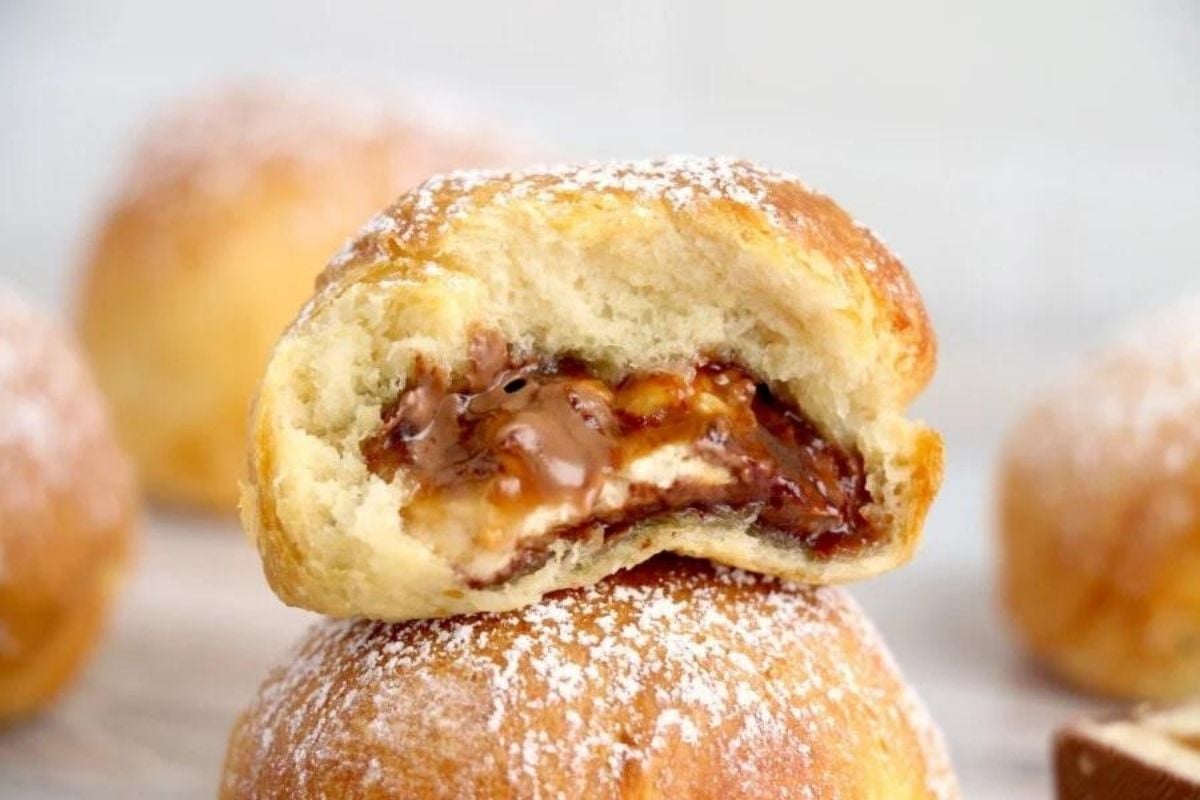 A close-up of a bitten doughnut filled with chocolate and dusted with powdered sugar, perfect for Father's Day breakfast.