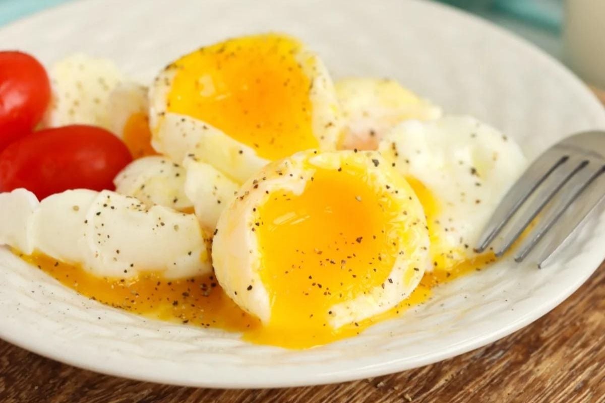 Poached eggs with runny yolks, seasoned with black pepper, served as a Father's Day breakfast with cherry tomatoes on a white plate.