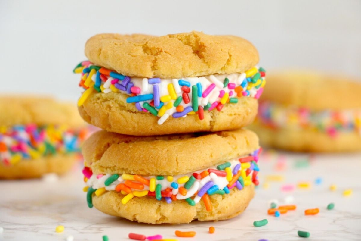 Two vanilla ice cream sandwiches with rainbow sprinkles on a light surface, perfect for pie recipes.