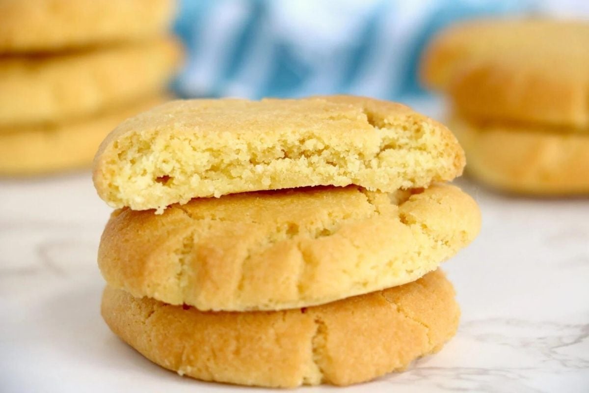 A stack of three golden-brown sugar cookies from our cookie recipes, with the top one broken in half to reveal a soft texture inside.