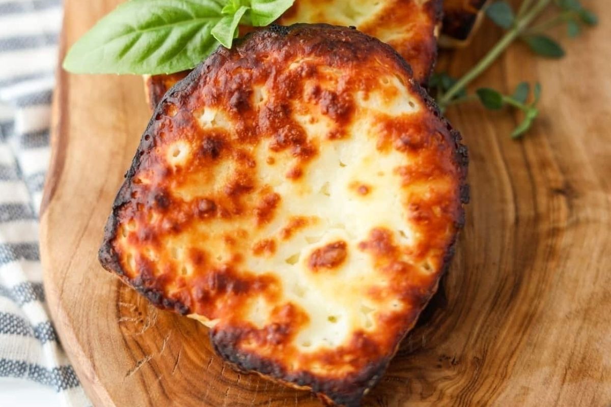 Cheesy grilled slices of halloumi cheese on a wooden board garnished with basil leaves.