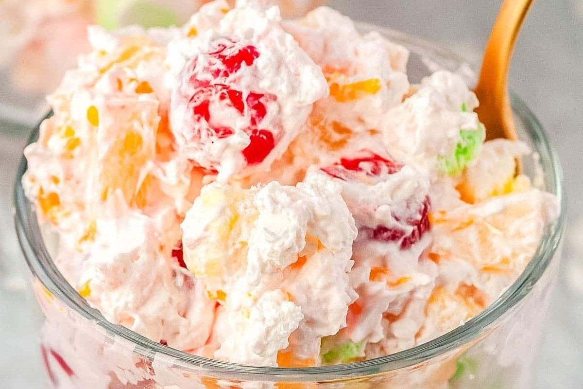 Fruit and jello salads in a glass bowl with a spoon.