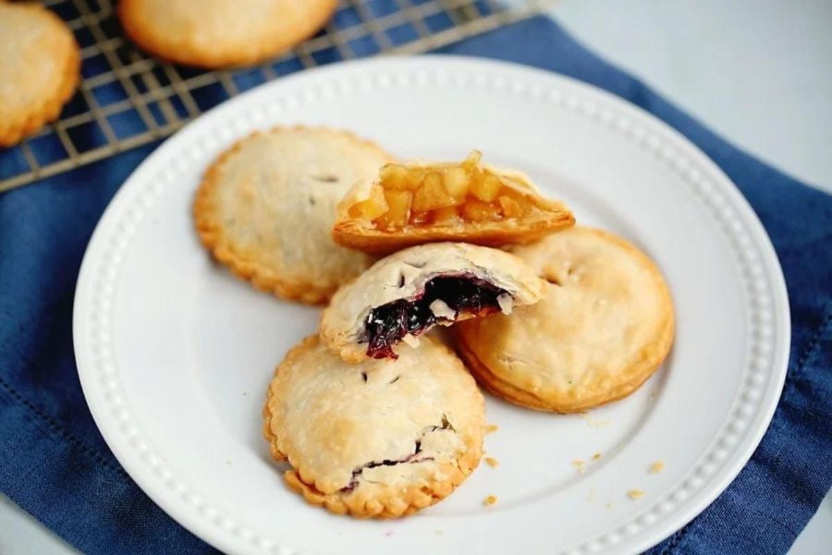 Plate of assorted fruit pie recipes with one pie cut open to show filling.