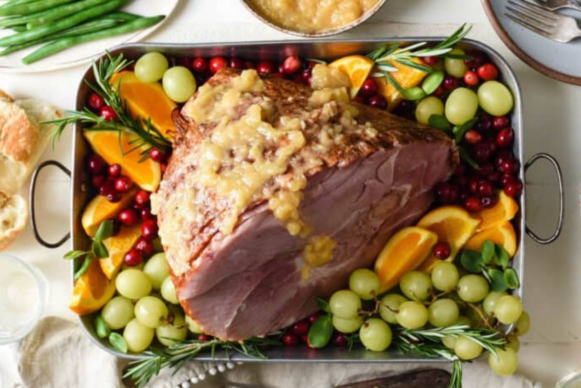 An Easter dinner featuring a glazed ham surrounded by fresh fruits and green beans on a dining table.