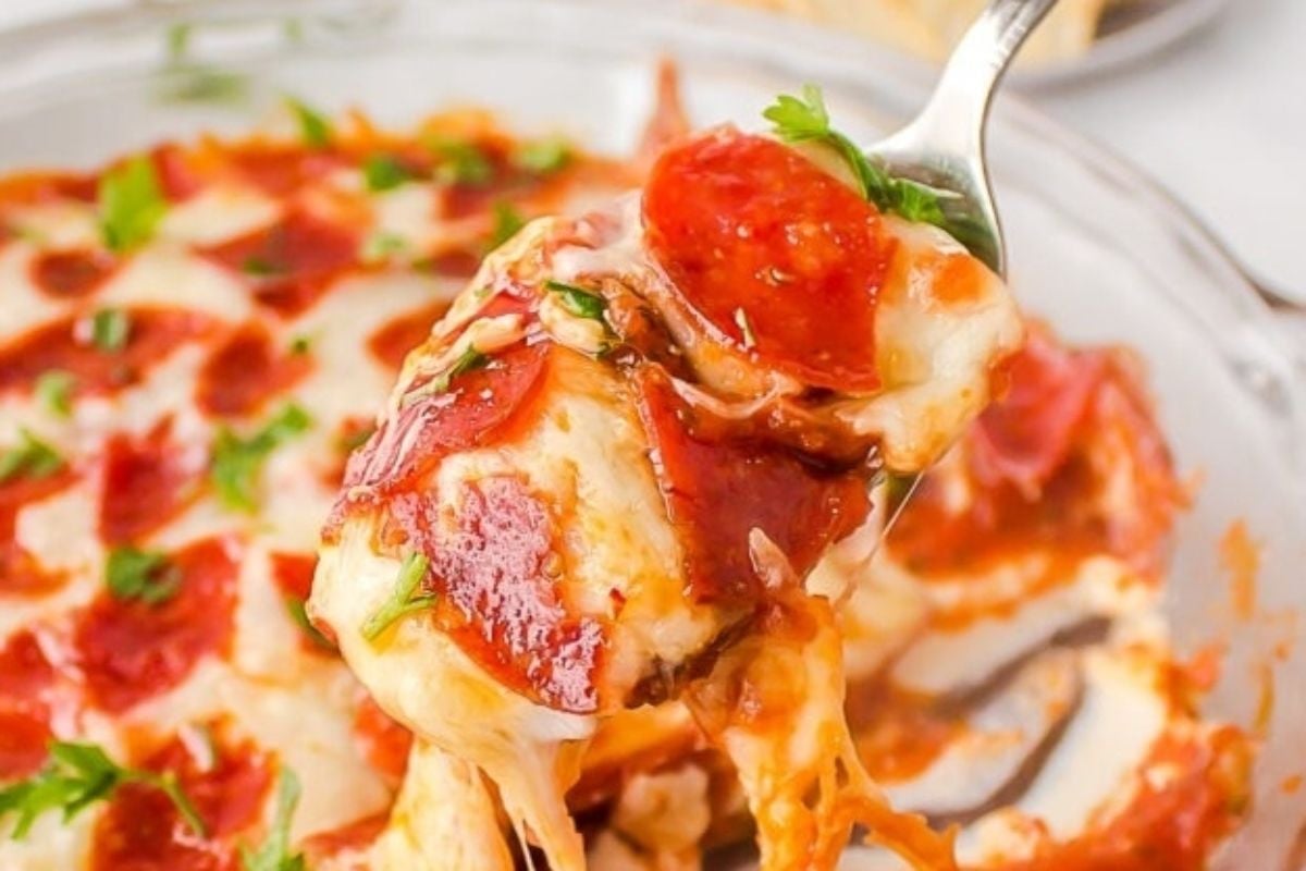 A fork lifts a cheesy, pepperoni-topped bite from a baked pizza casserole dish—a delicious example of easy, cheesy recipes.