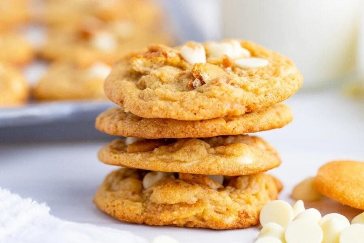 Stack of freshly baked white chocolate chip cookies from our cookie recipes with a glass of milk in the background.