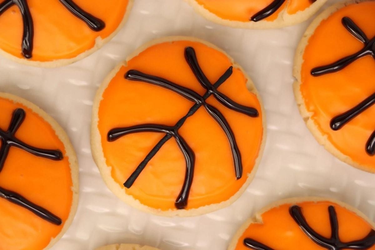 Cookies decorated with orange icing and a chocolate drizzle resembling a basketball pattern, perfect for cookie recipes.