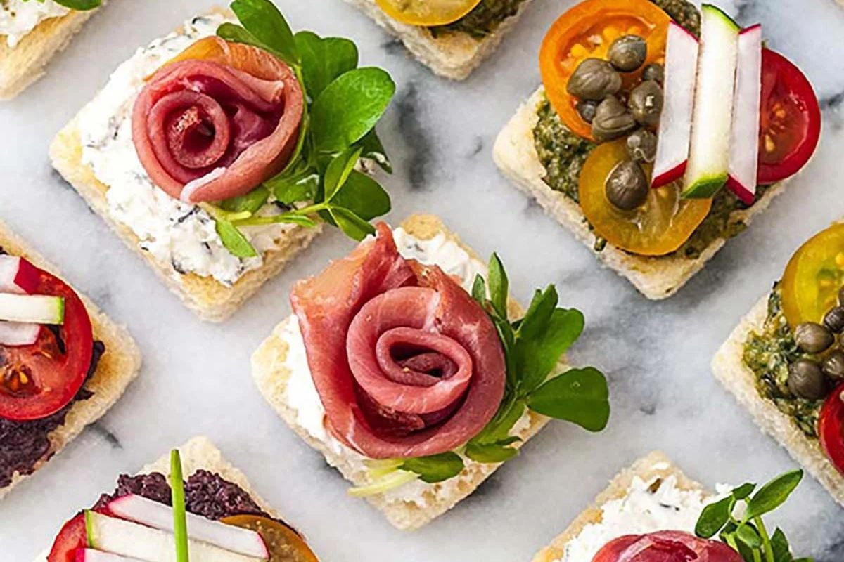An assortment of elegant Easter appetizers with various toppings on square crackers arranged on a marble surface.