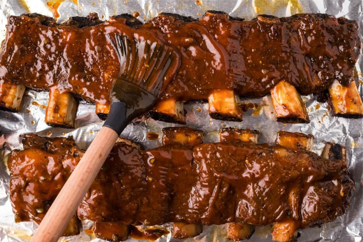Easy rib recipes: Glazed barbecued ribs being brushed with sauce on aluminum foil.