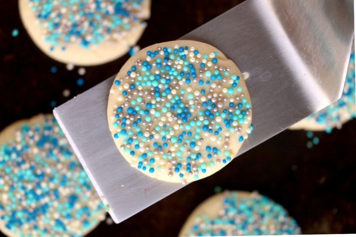 A spatula lifting a cookie, adorned with blue and white sprinkles and perfect for various cookie recipes.
