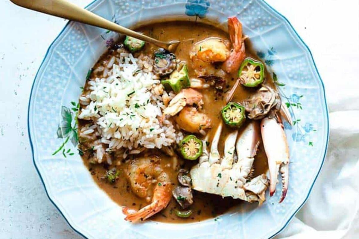 A plate of seafood gumbo from our seafood recipes, with shrimp, crab legs, and rice, garnished with sliced jalape&ntilde;os and herbs.