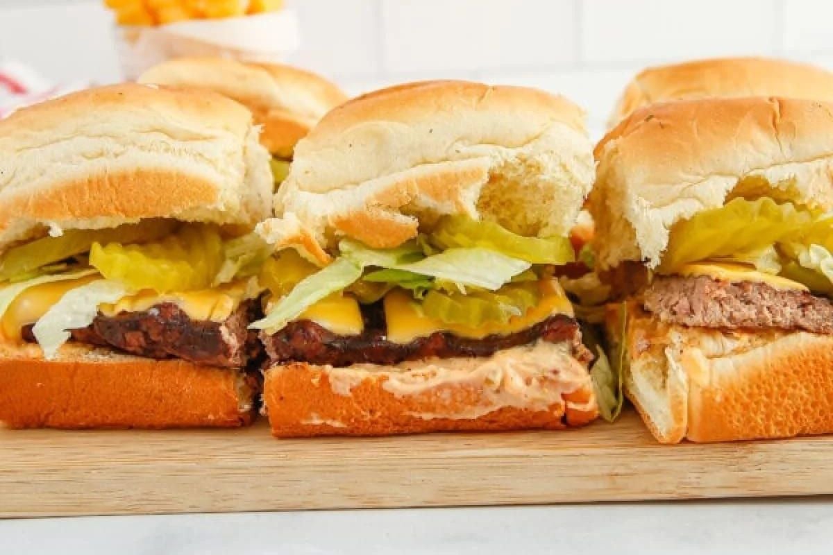 Three slider recipes with pickles and lettuce on a wooden board.
