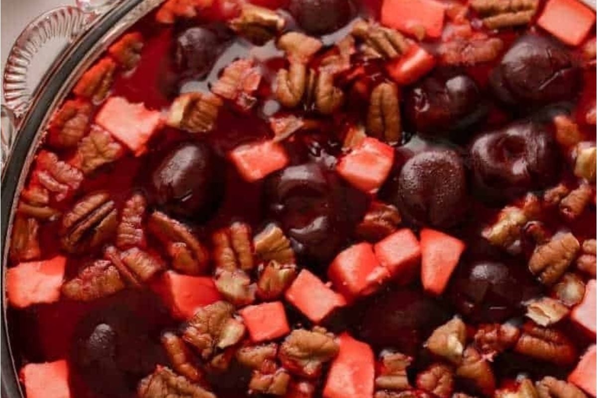 A glass bowl filled with jello salads, cherries, and pecans.