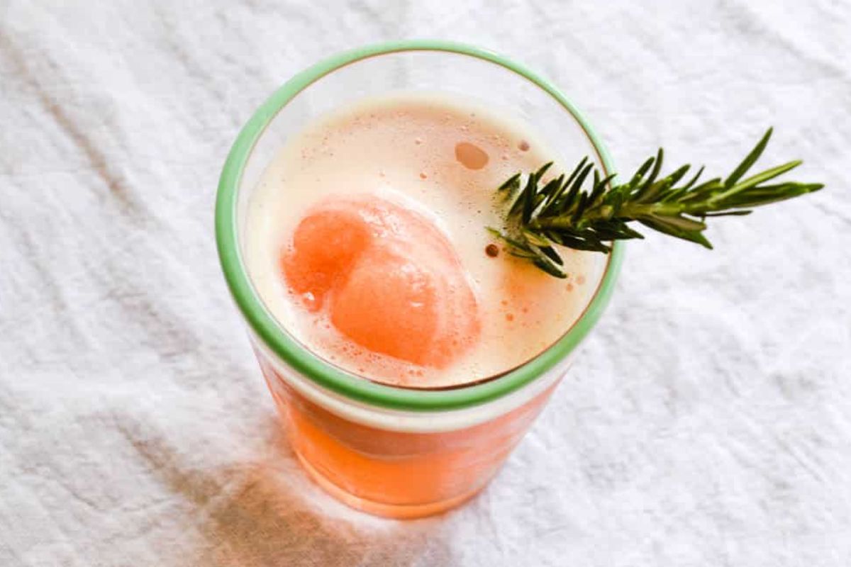 A glass of pink Easter cocktail with a sprig of rosemary and an ice sphere.