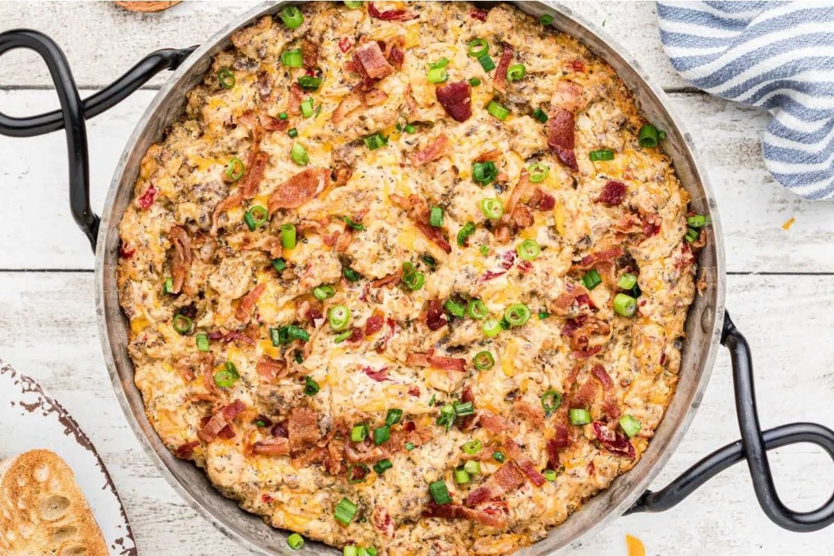 A baked breakfast casserole packed with cheesy goodness, topped with chopped green onions and bacon in a round pan on a white table—perfect for fans of cheesy recipes.
