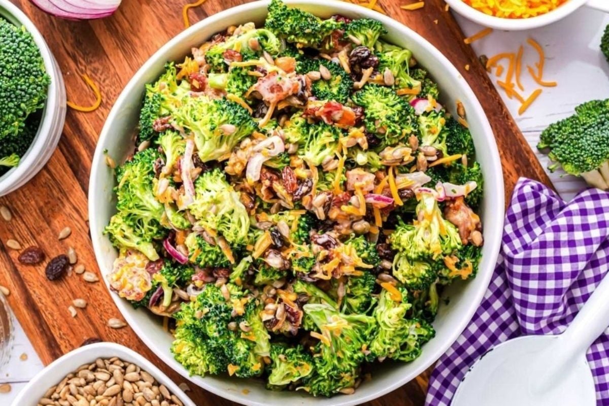 A bowl of broccoli salad, perfect for potluck sides, on a wooden cutting board.
