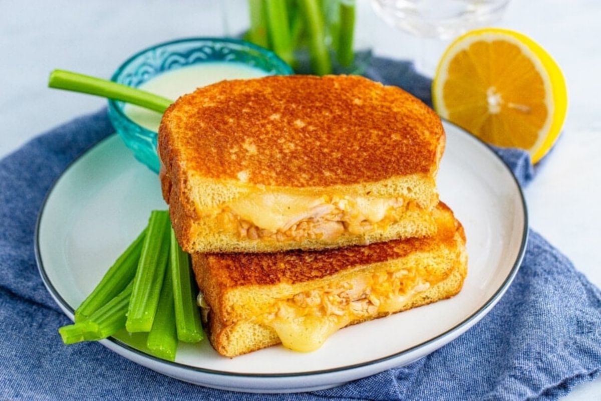 Grilled cheese sandwich, a cheesy recipes staple, cut in half on a plate with green onions and a lemon slice.