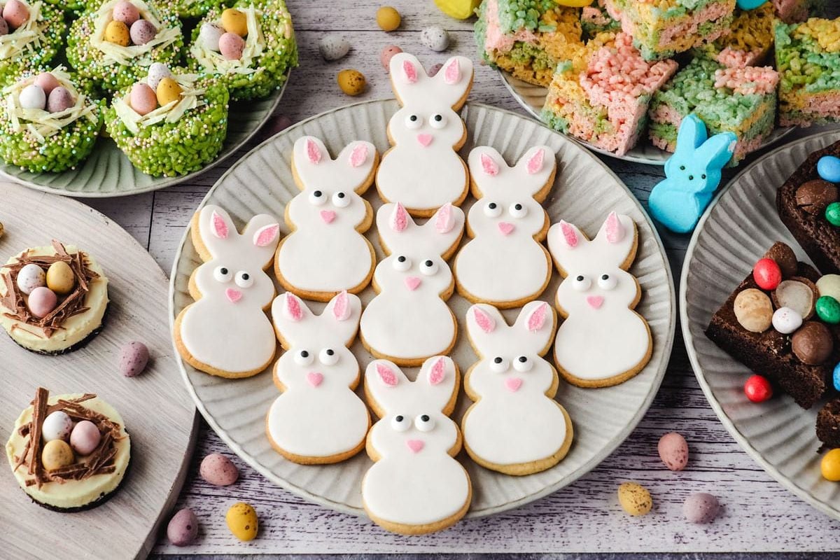 Assorted Easter-themed treats on a table, including iced Easter cookies, chocolate nests with eggs, and colorful rice cereal treats.