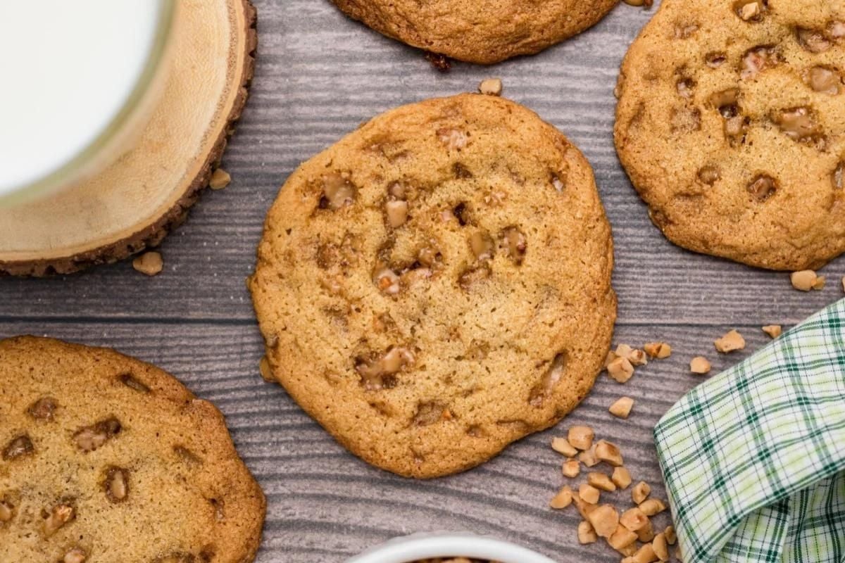 Chocolate chip cookie recipes on a wooden surface with a glass of milk and scattered nuts.