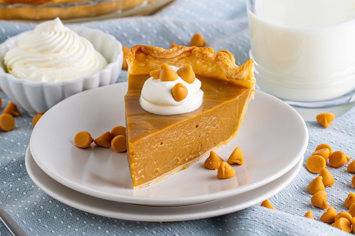 A slice of pumpkin pie topped with whipped cream and butterscotch chips, accompanied by a glass of milk and more whipped cream, is a highlight in pie recipes.