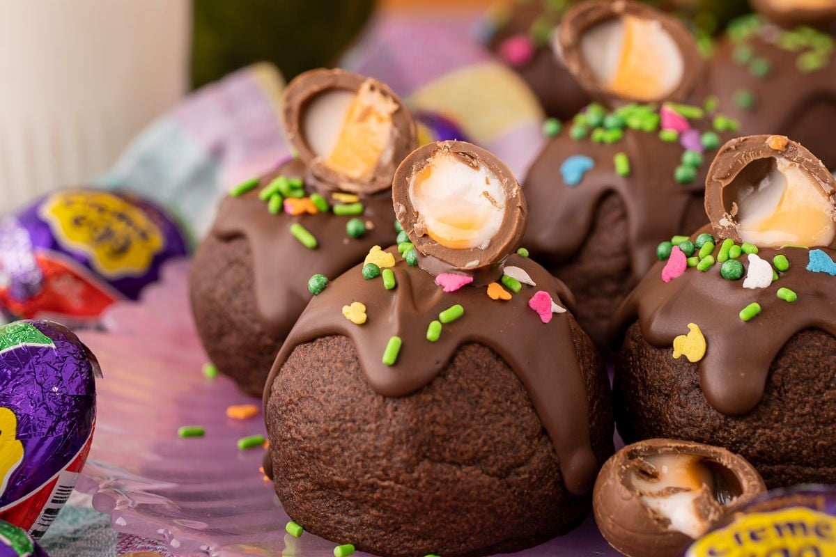 Chocolate cupcakes topped with melted chocolate, colorful sprinkles, and half of an Easter cookie.