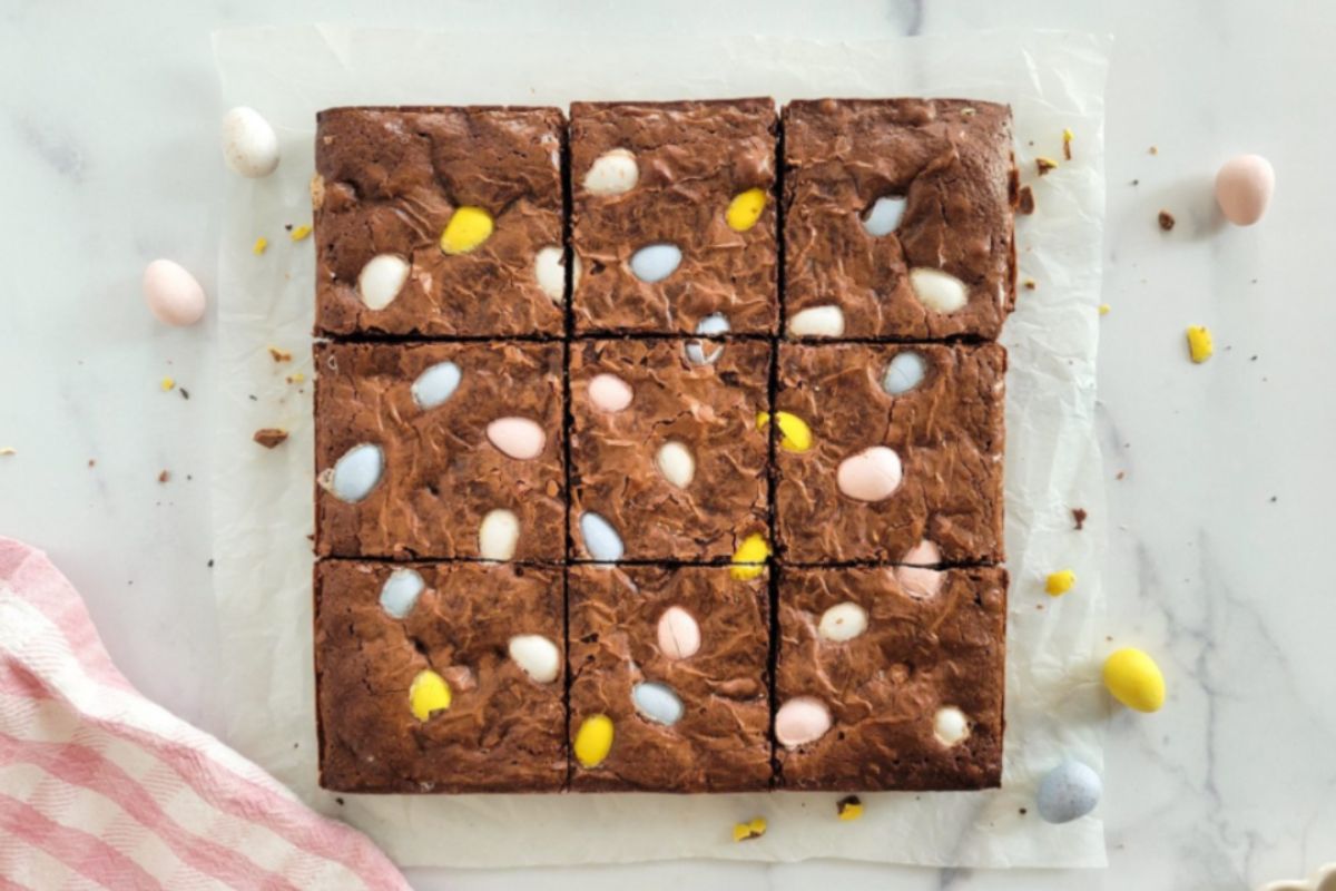 A batch of freshly baked brownies with colorful candy toppings, cut into squares and presented on parchment paper as Easter desserts.
