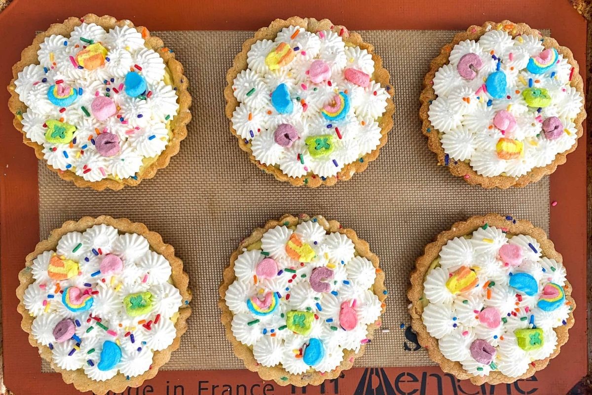 A tray of cupcakes with Lucky Charms, whipped cream, and sprinkles.