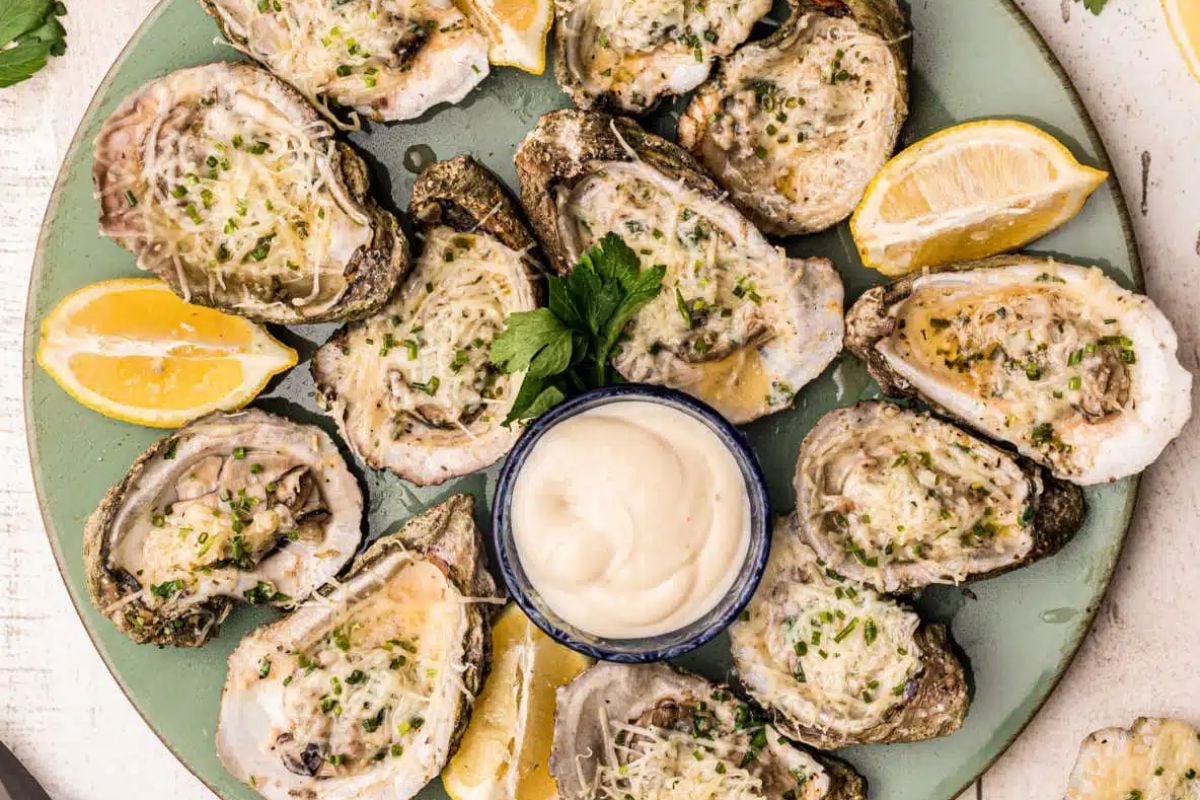 A plate of freshly shucked oysters, a highlight in seafood recipes, garnished with lemon wedges and herbs, served with a side of sauce.