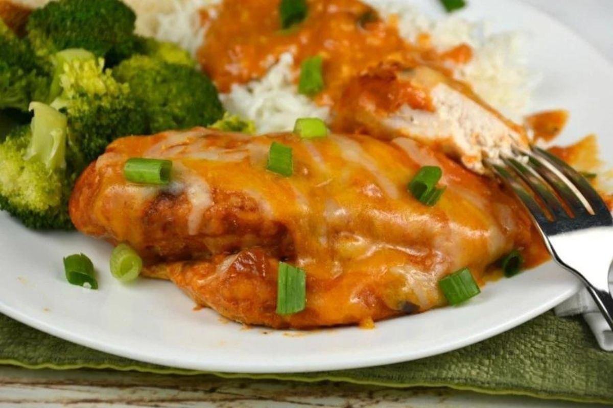 Plate of chicken enchiladas topped with extra cheese and green onions, served with broccoli and mashed potatoes.