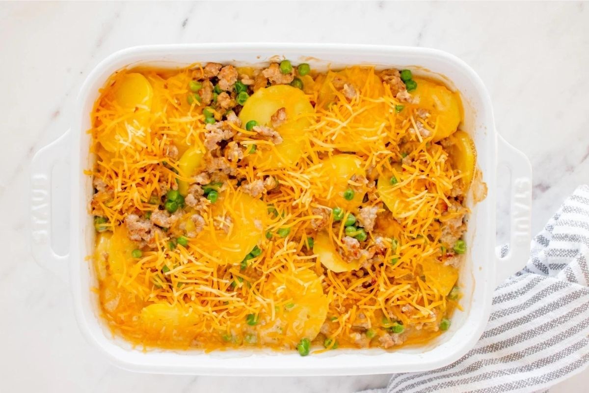 A cheesy baked casserole with ground meat, sliced potatoes, peas, and melted cheese topping.
