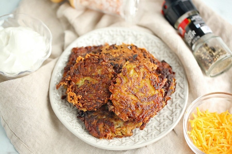 Plate of crispy potato hash browns served with sour cream and shredded cheese on the side.