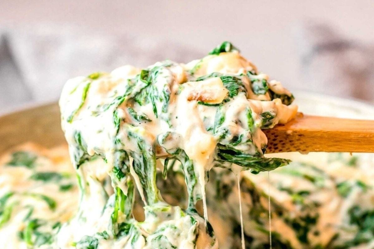A wooden spoon lifting creamy spinach and cheese from a bowl, showcasing the stringy, melted texture perfect for cheesy recipes.