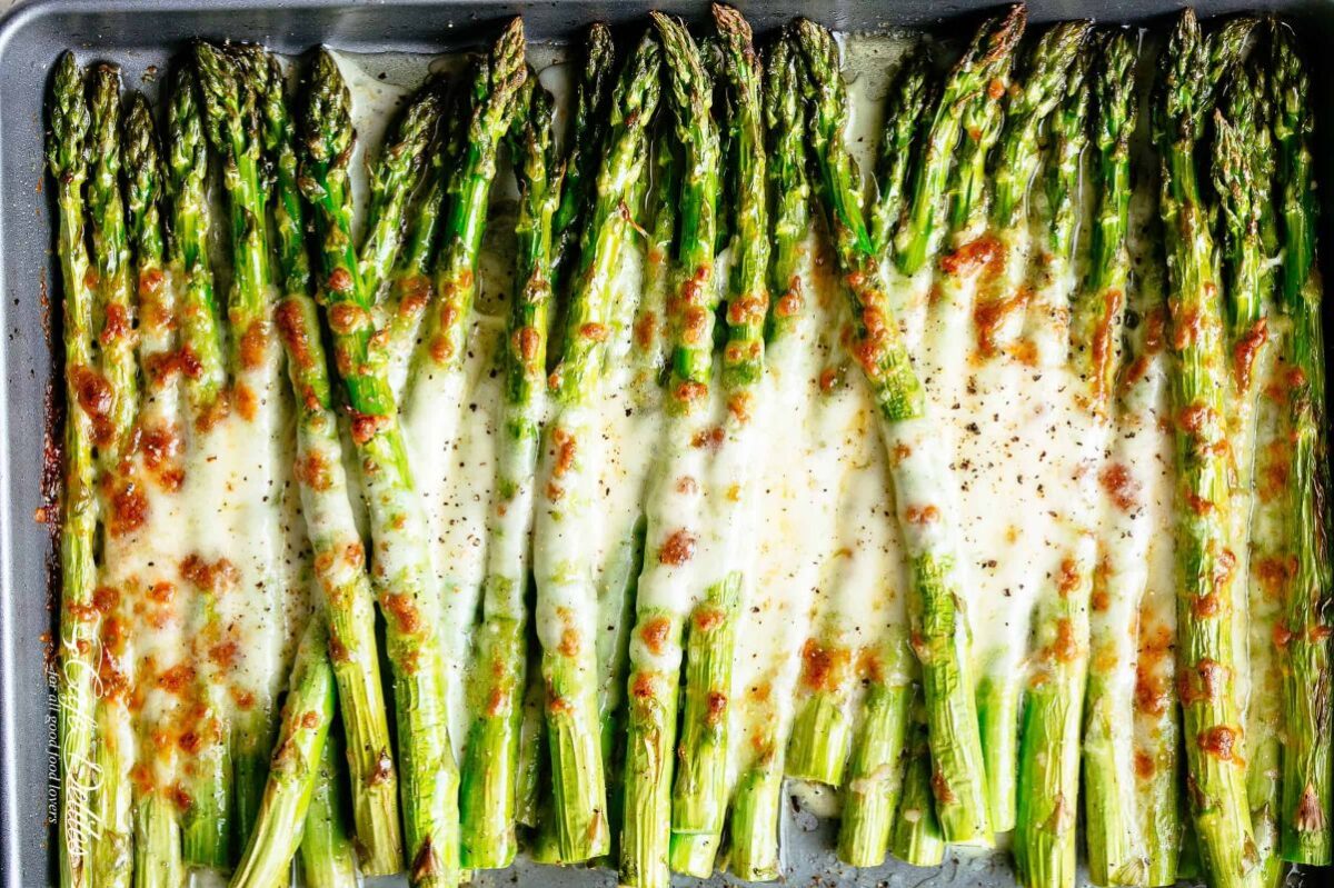 Roasted asparagus with melted cheese and seasoning on a baking sheet, perfect for Easter dinner.