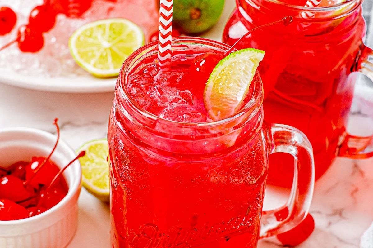 A refreshing Easter cherry limeade cocktail in a mason jar with a straw, surrounded by limes and cherries.